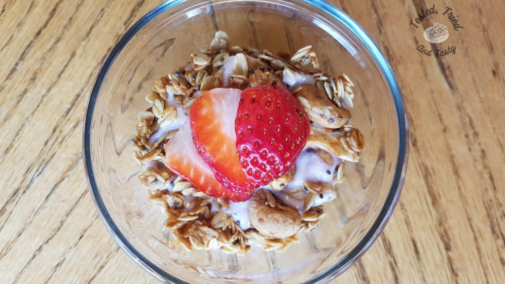 homemade granola in a glass bowl with yogurt and a strawberry.