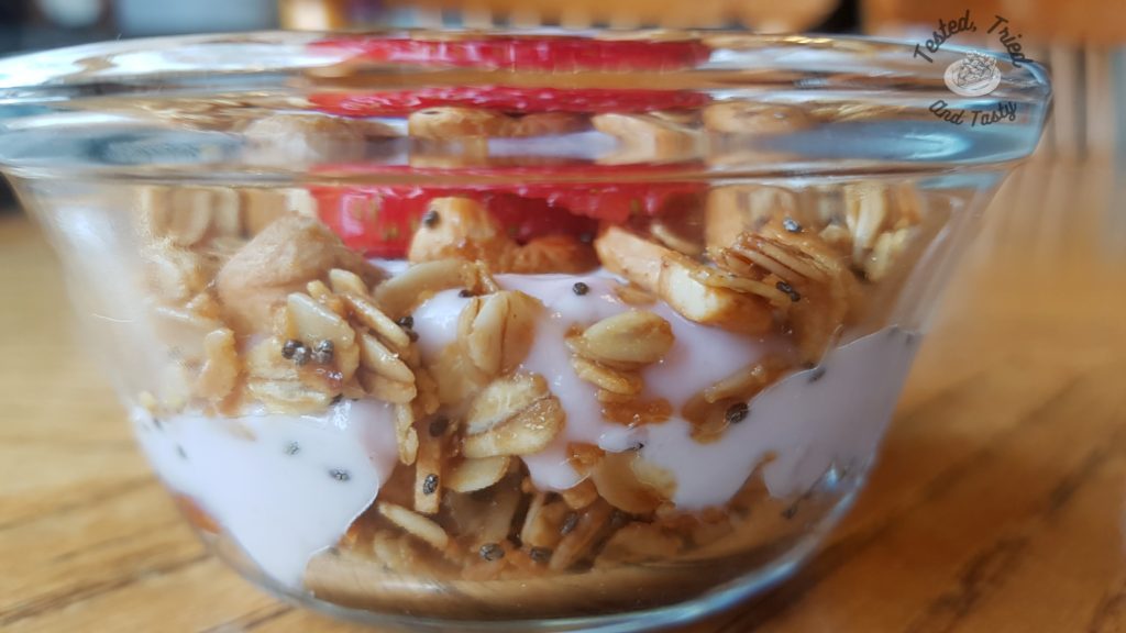Crunchy, Healthy, Quick and Easy Granola in a glass bowl with yogurt and a strawberry.