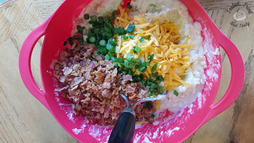 Potaoes with bacon, green onions and cheddar cheese in a red bowl on a wood table, the filling for fully loaded stuffed potatoes recipe.