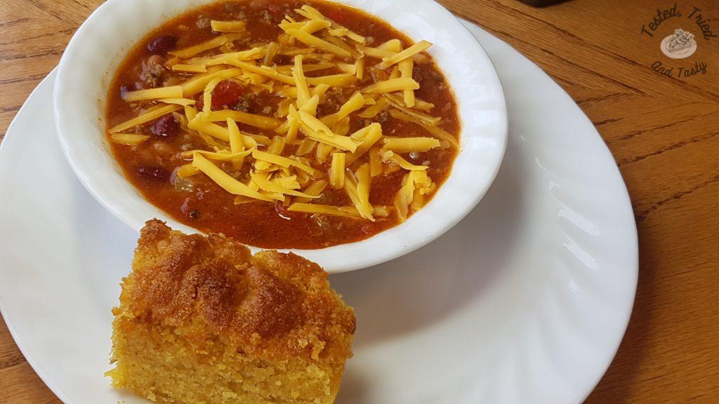 Homemade classic chili with cheddar cheese accompanied by Buttermilk Graham Cornbread on a white plate