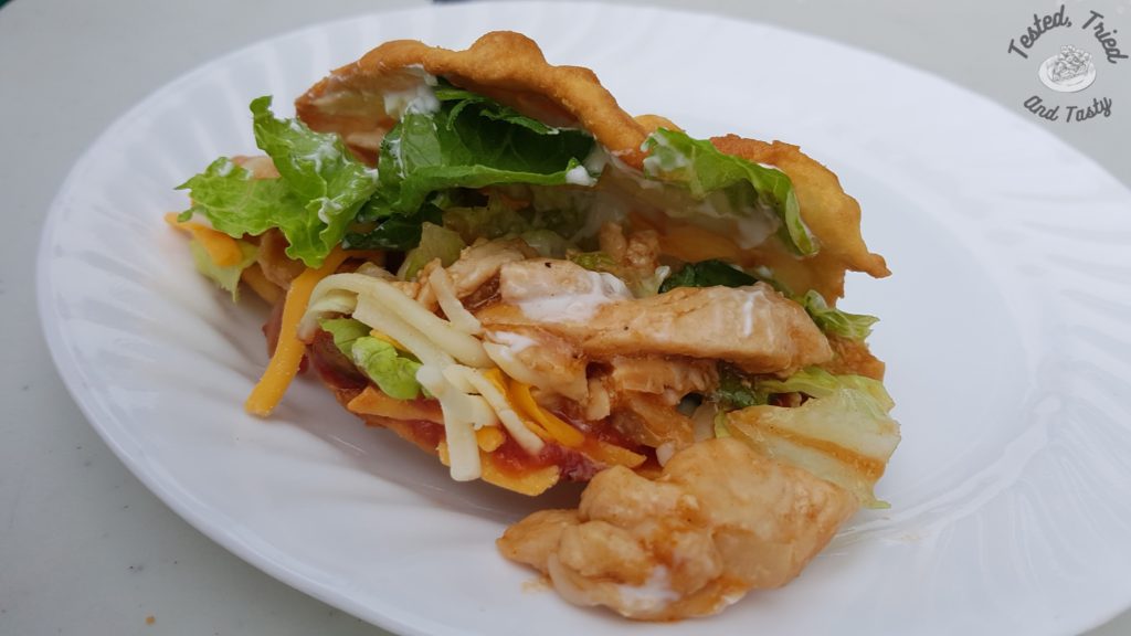 barbecue chicken frybread taco with lettuce cheese salsa on a white plate