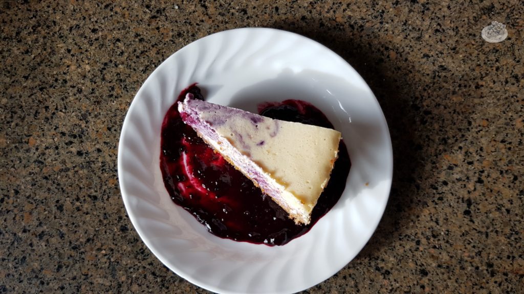 Blueberry Cheesecake with gingersnap crust on a white plate on a marble countertop.