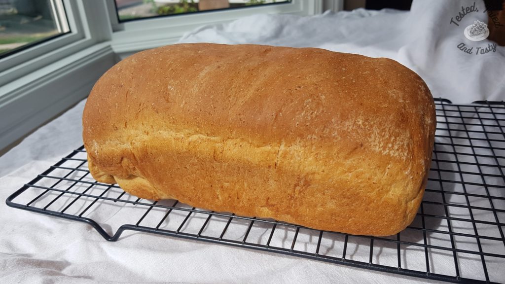 Almost Whole wheat bread on a wire cooling rack on a white tablecloth.