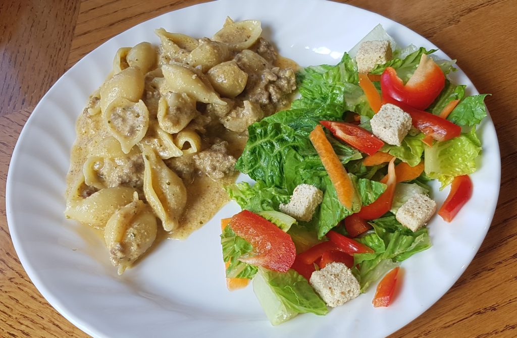 Cheesy homemade hamburger helper with a salad on a white plate.