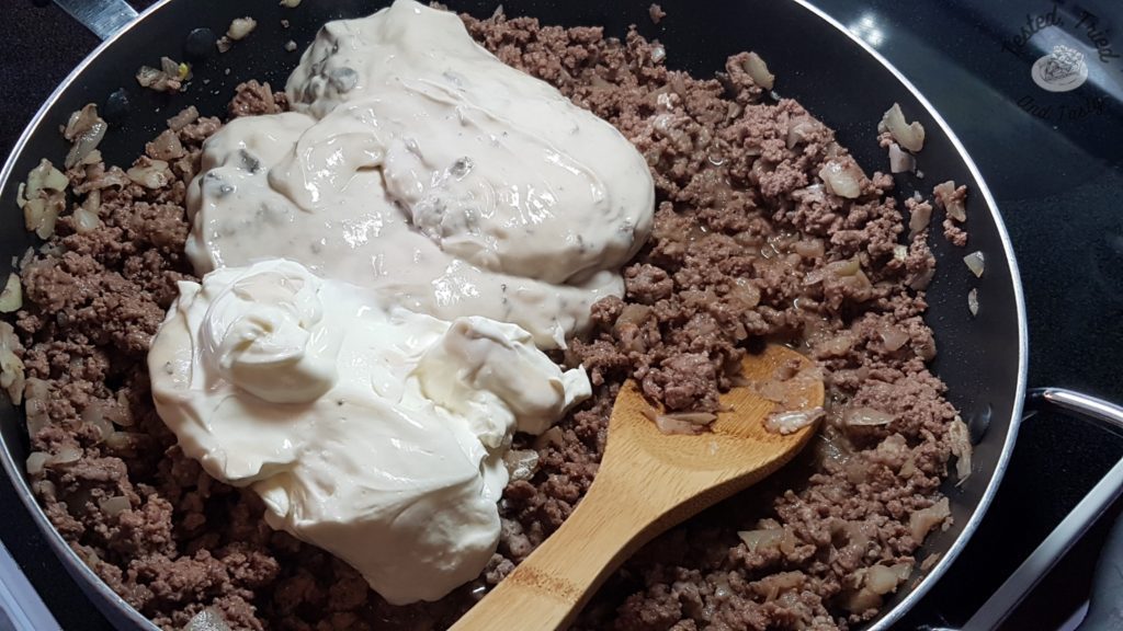 mushroom soup and sour cream being added to extra lean ground beef and onions in a frying pan.