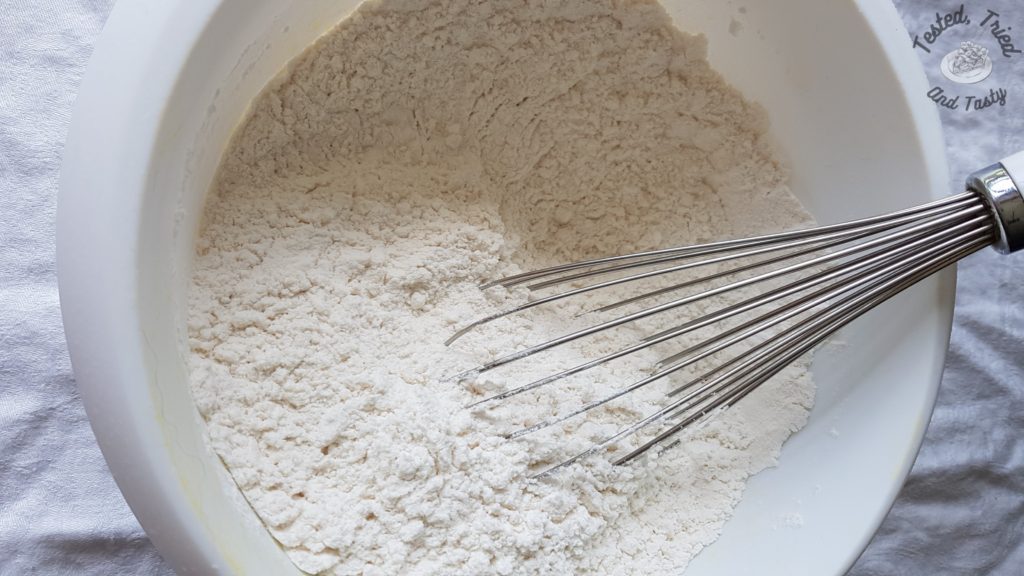 dry ingredients for vanilla cupcakes in a white bowl with a whisk.