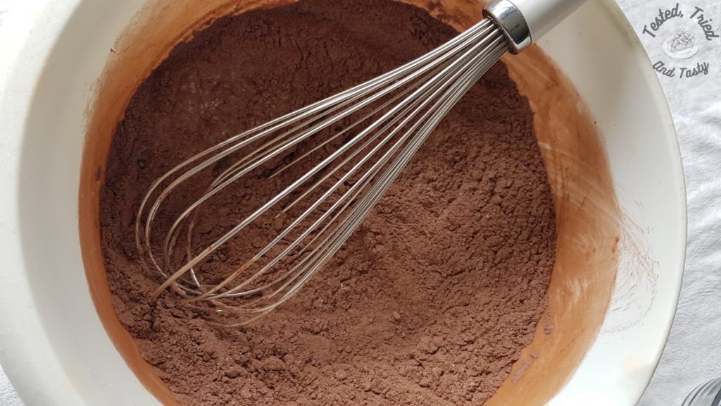 dry ingredients for chocolate cupcakes being whisked in a white bowl,