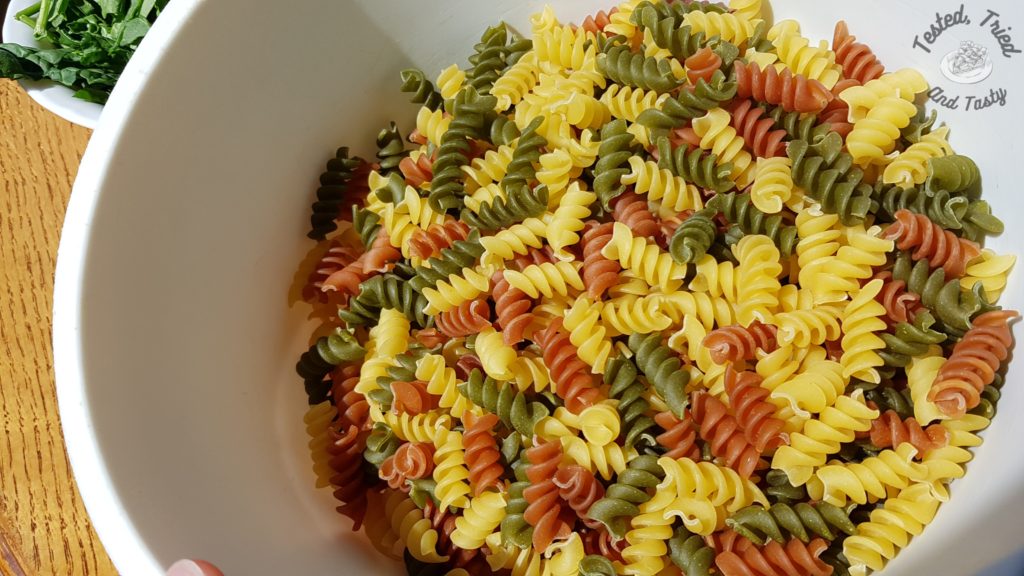 Tri color Rotini in a white bowl on a wooden table.