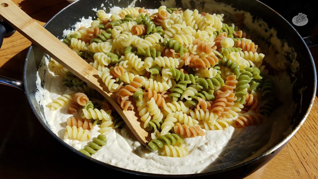 Cooked rotini noodles added to garlic alfredo sauce in a saucepan.