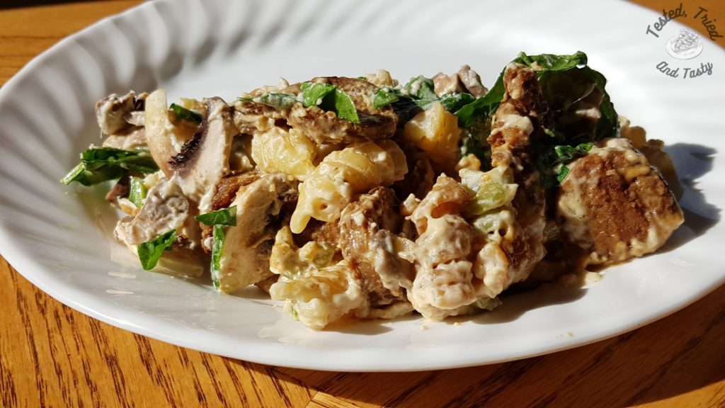 Garlic Sausage and Spinach Alfredo on a white plate on a wooden table.