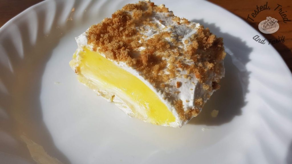 Lemon Lush Pudding Dessert on a white plate on a wooden table.