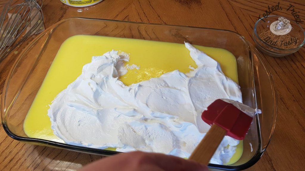 Spreading cool whip onto Lemon Lush Pudding Dessert.