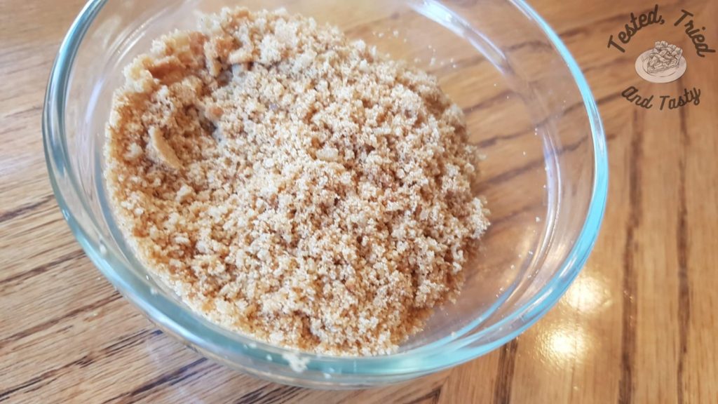 Crushed gingersnaps in a glass bowl on a wooden table.