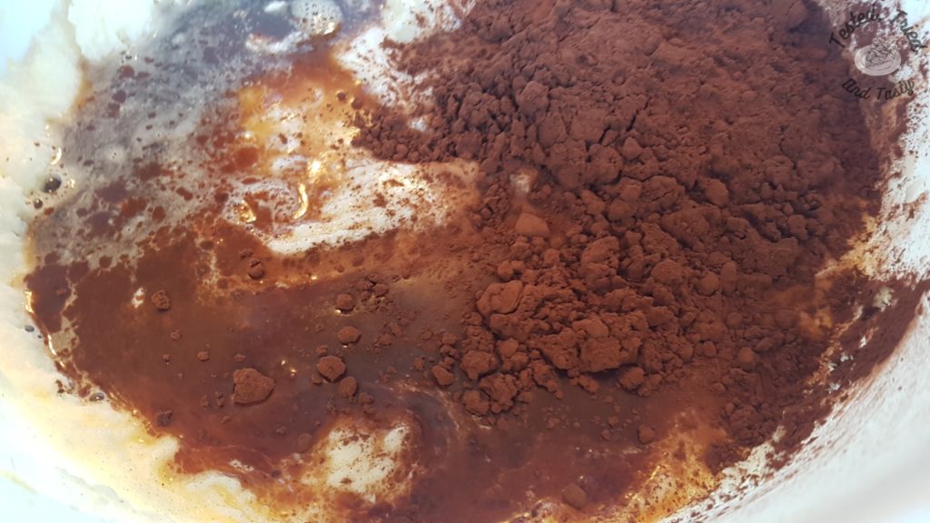 Cocoa powder added to the butter and sugar mixture in a white bowl.