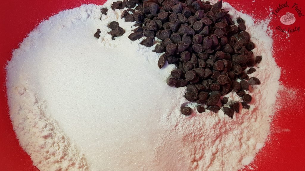 Flour, sugar, baking powder, salt and semi sweet chocolate chips in a red bowl.