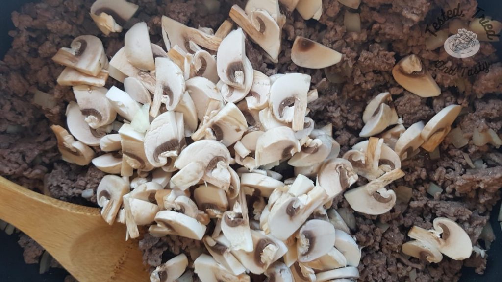 Mushrooms added to cooked ground beef in a large skillet.