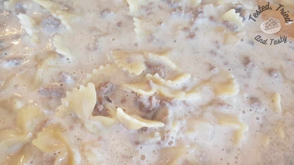 Pasta added to ground beef and mushrooms in a large skillet.