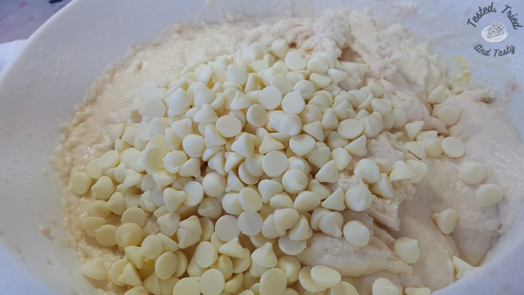 White chocolate chips added to the muffin batter in a white bowl.