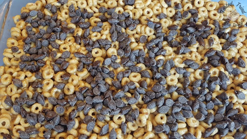 Chocolate chips sprinkled on the top of peanut butter cheerio bars.