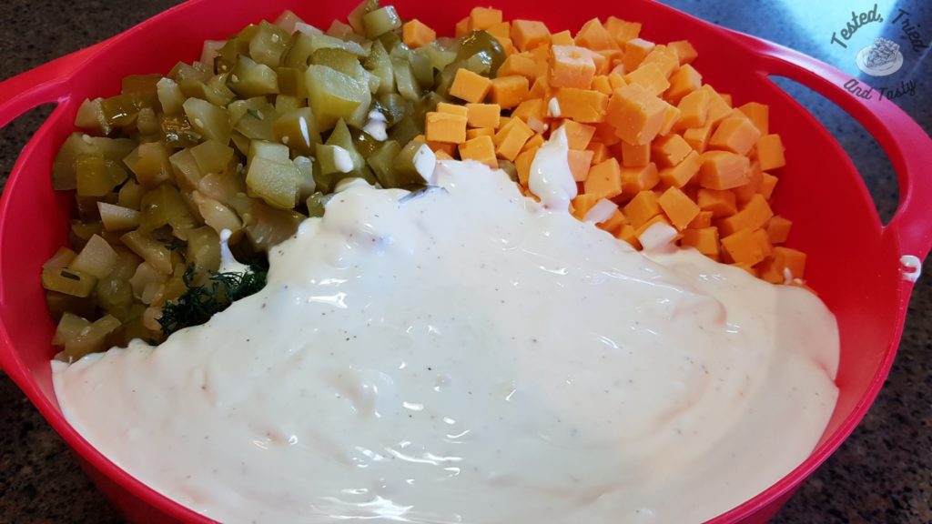 Dressing poured onto the ingredients for dill pickle pasta salad.