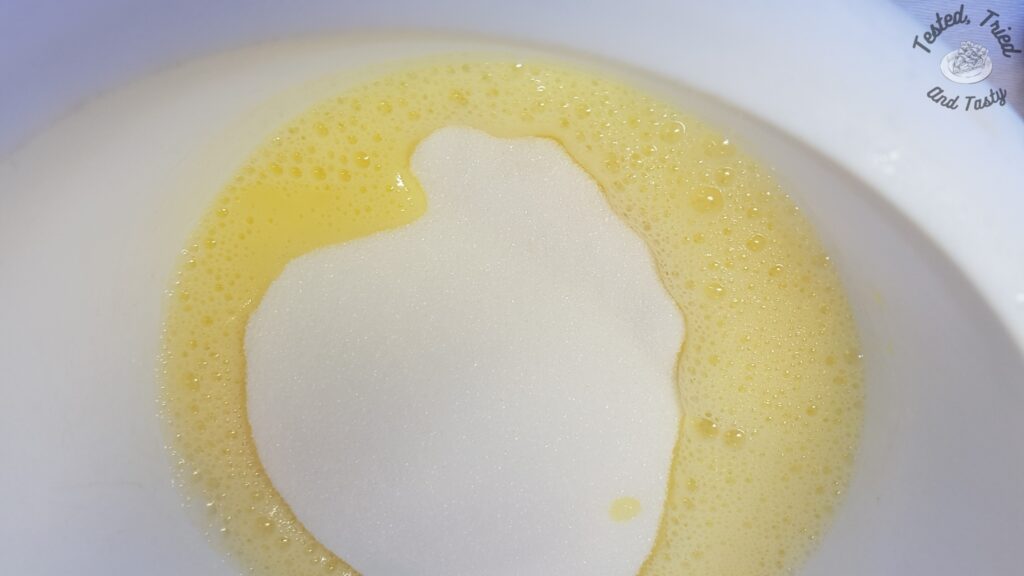 Granulated sugar added to beaten eggs in a white bowl.