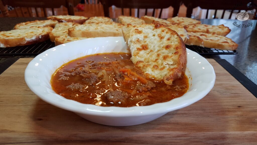 Homemade Hamburger soup in a white bowl with a slice of garlic bread.