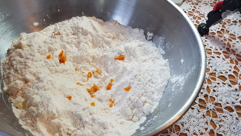 Orange zest added to dry ingredients in a large silver bowl.