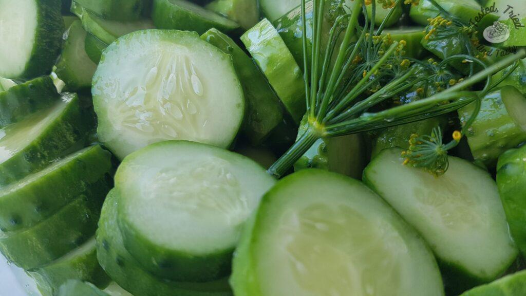 Dill, garlic and sliced cucumbers in a plastic buckent.