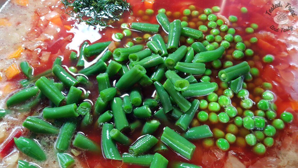 Peas and beans added to beet borscht in a large saucepan.