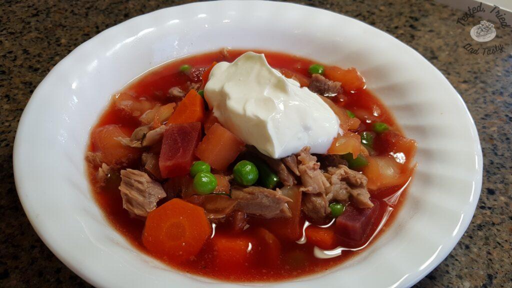 Beet borscht recipe in a white bowl, with a dollop of sour cream.