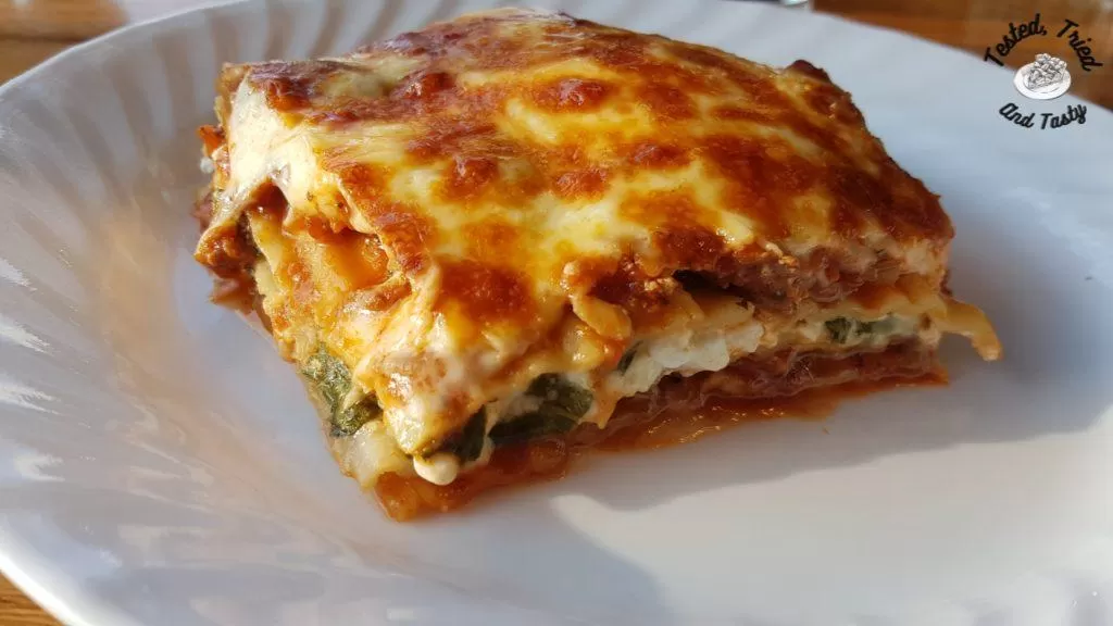 Tasty baked lasagne on a white plate.