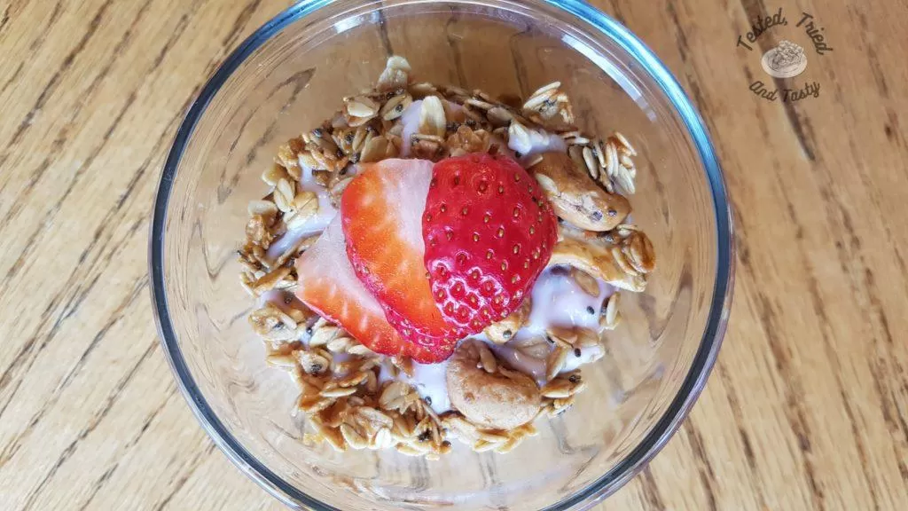 homemade granola in a glass bowl with yogurt and a strawberry.