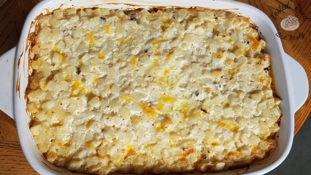 Deluxe and Creamy hashbrown casserole in a white casserole dish.