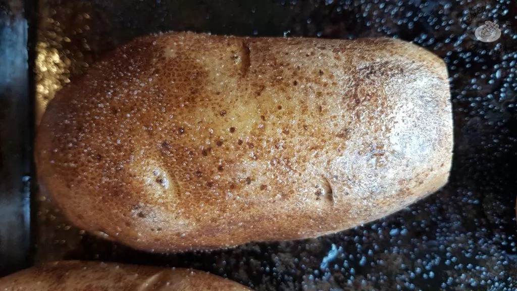 A baked potato on a baking sheet, ready for fully loaded stuffed potatoes recipe.