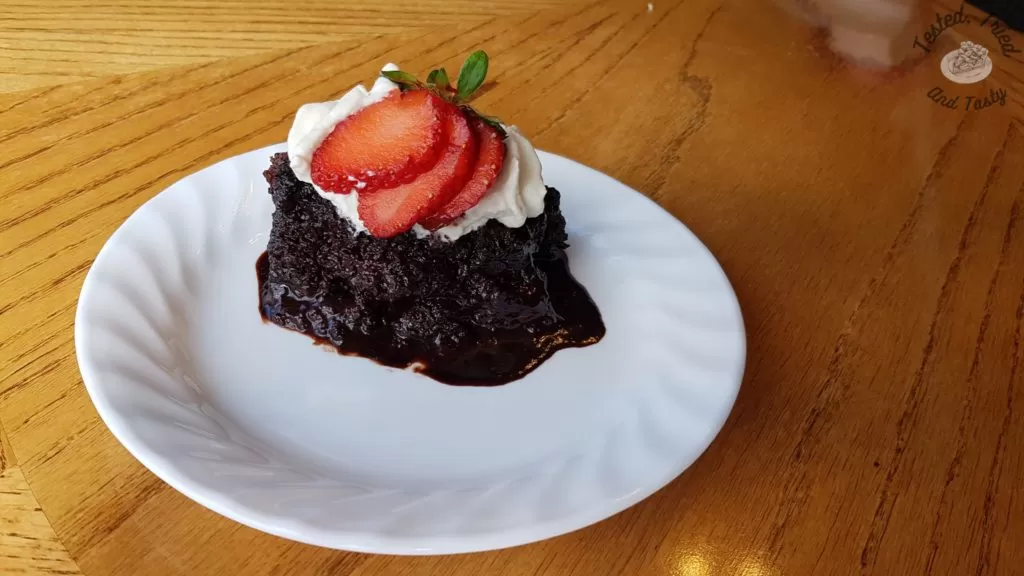 Chocoholic Pudding Cake with whipped cream and strawberry on a white plate.