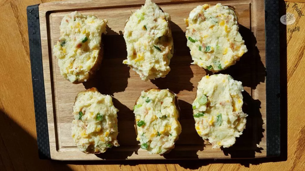 Fully loaded stuffed potatoes on a wooden cutting board.