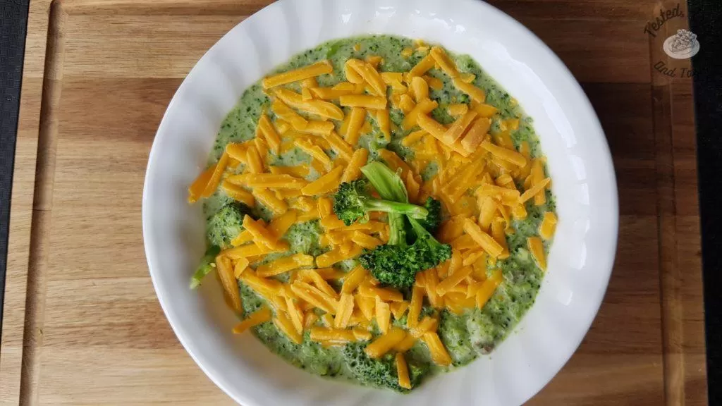 Homemade Cream of broccoli soup with cheddar cheese on a wood cutting board.