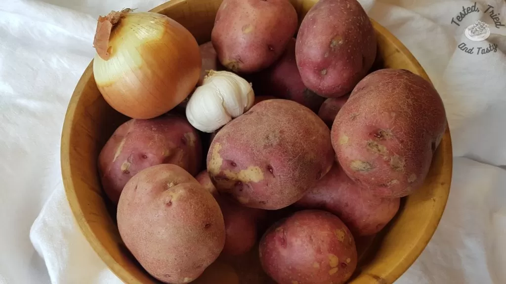 Red potatoes, onion and garlic in a wood bowl on a white tablecloth.