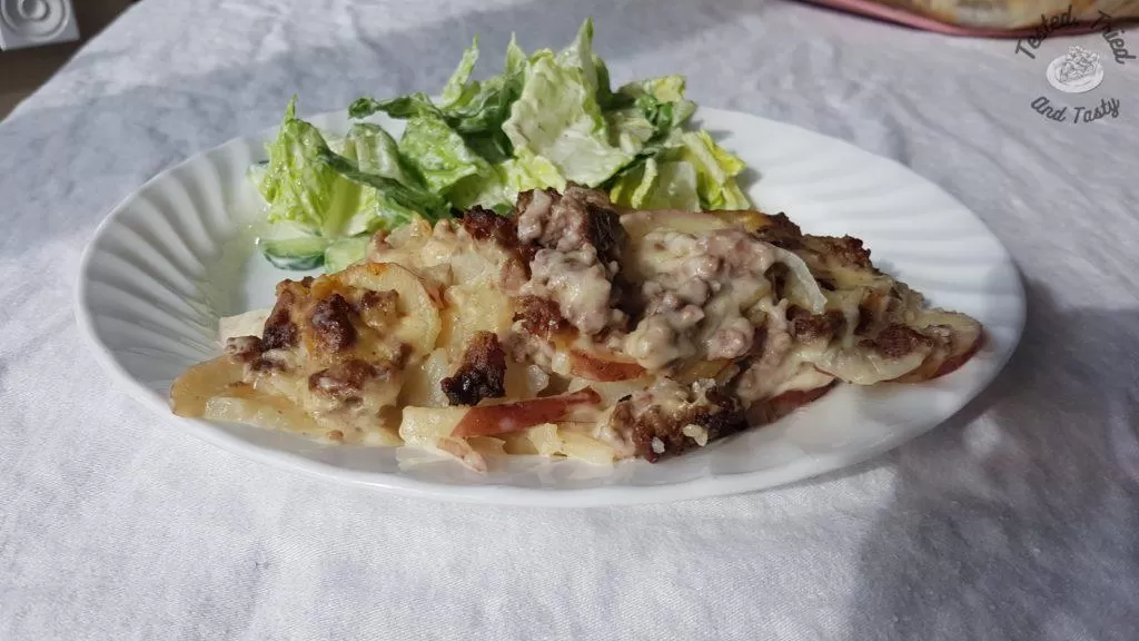 Beefy scalloped potatoes on a white plate on a white tablecloth.