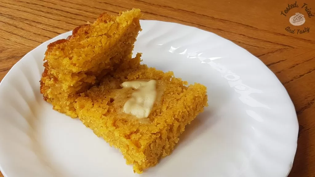 Buttermilk Graham Cornbread with butter on a white plate on a wood table.