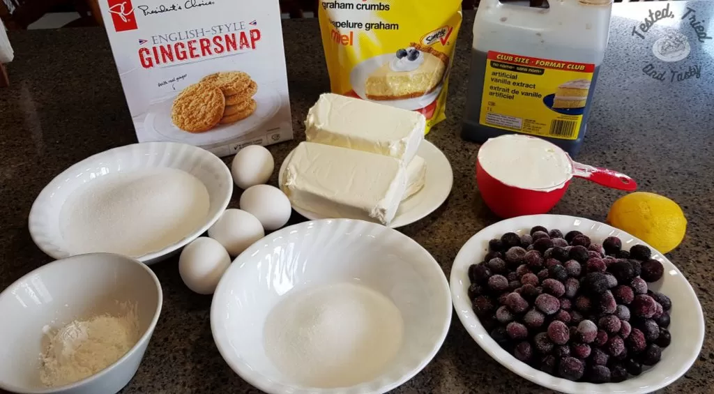 ingredients for blueberry cheesecake with a gingerbread crust. Gingersnaps, graham crumbs, sugar, butter, cornstarch, eggs, cream cheese, sour cream, vanilla, blueberries, lemin juice.