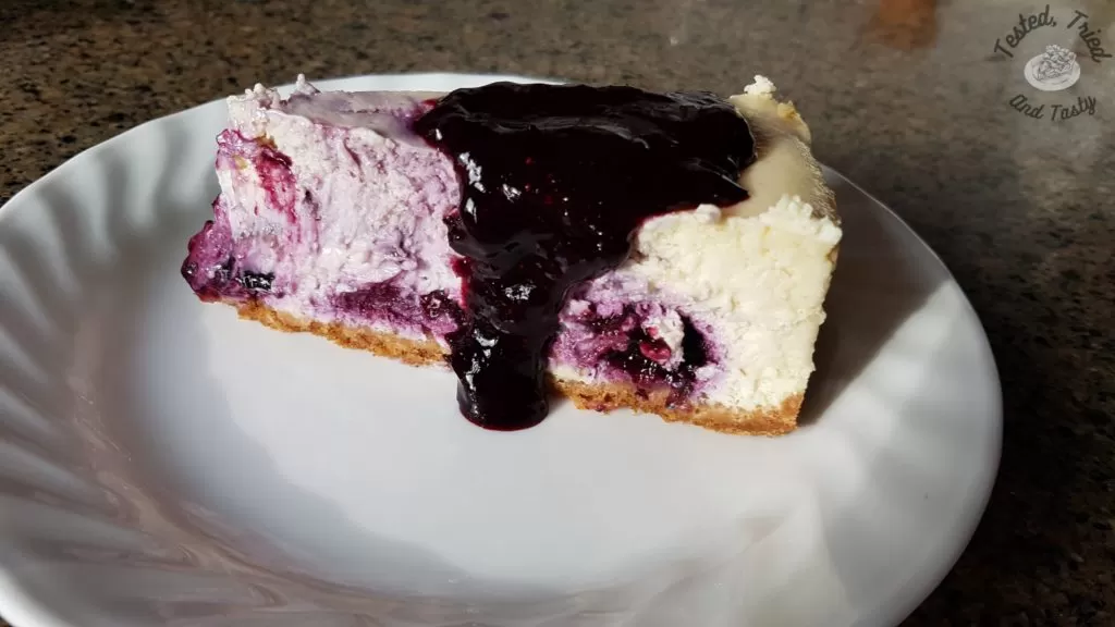 blueberry cheesecake with a gingersnap crust on a white plate on a granite countertop