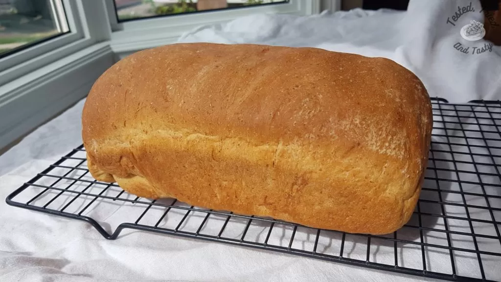 Almost Whole wheat bread on a wire cooling rack on a white tablecloth.