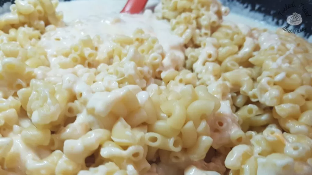 Stirring the pasta into the creamy cheese sauce for Baked Mac and Cheese recipe.