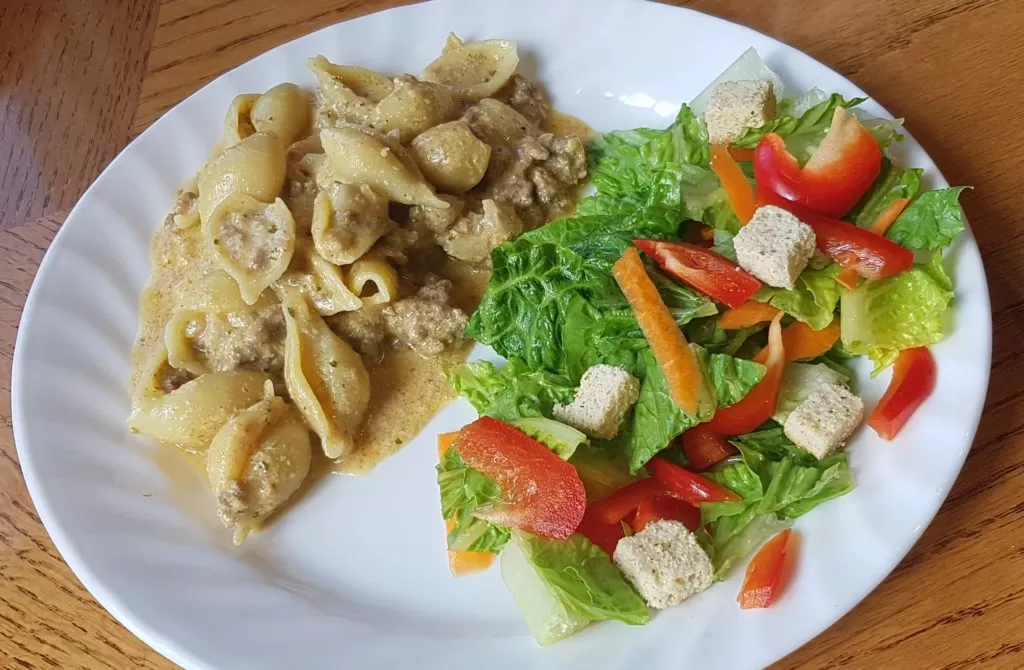 Cheesy homemade hamburger helper with a salad on a white plate.