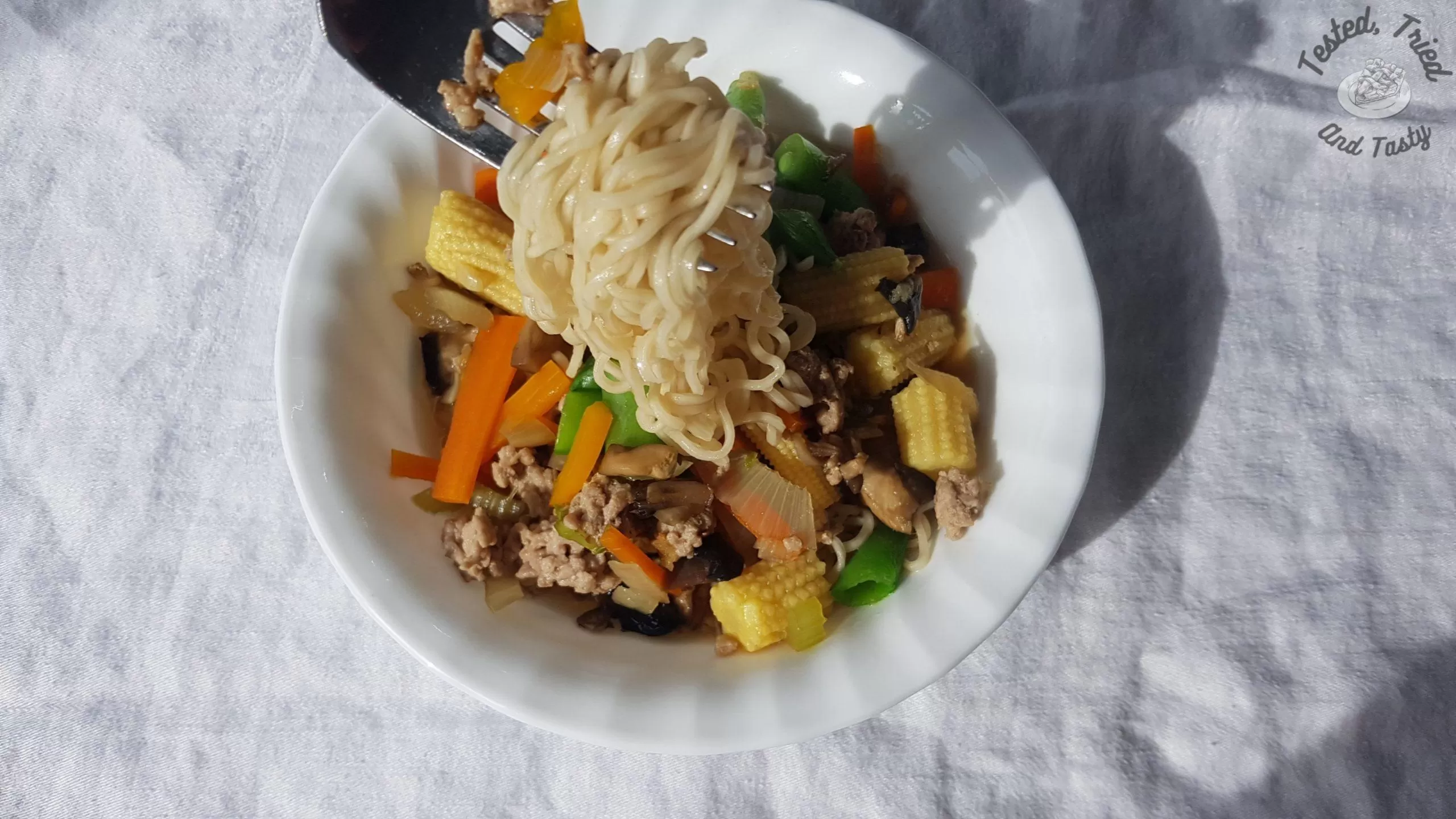 Oriental Pork and Noodle Soup in a white bowl on a white tablecloth.