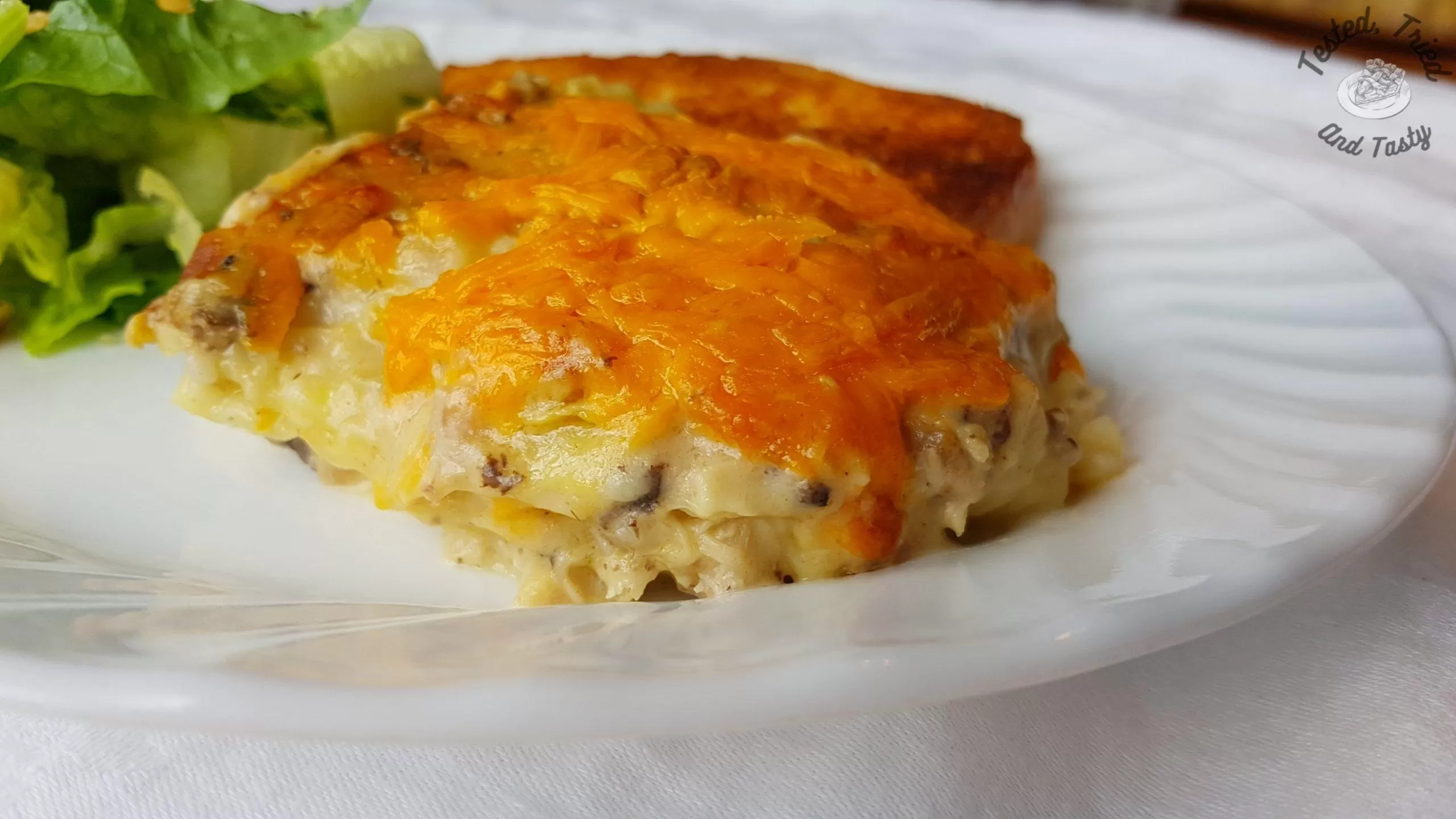 creamy chicken lasagne with salad and garlic bread on a white plate
