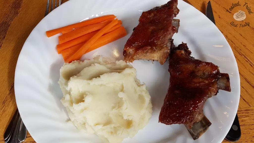 mouthwatering sweet and smoky barbecue ribs, creamy mashed potatoes and carrot sticks on a white plate.