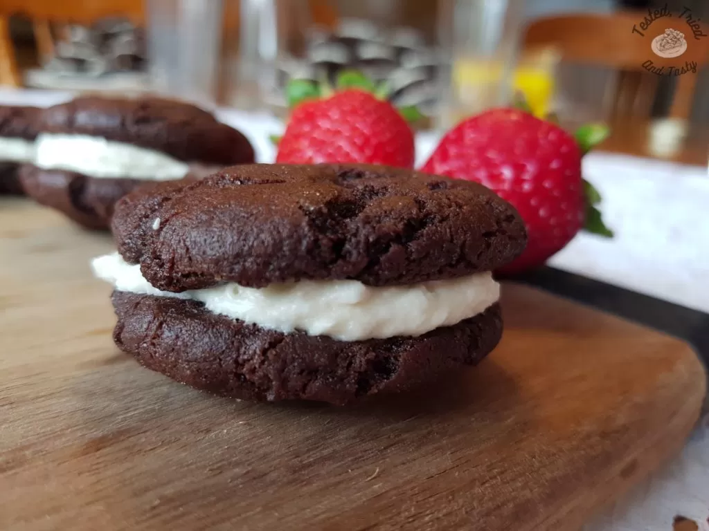 homemade oreo cookies with stawberries on a wooden cutting board on a white tablecloth.