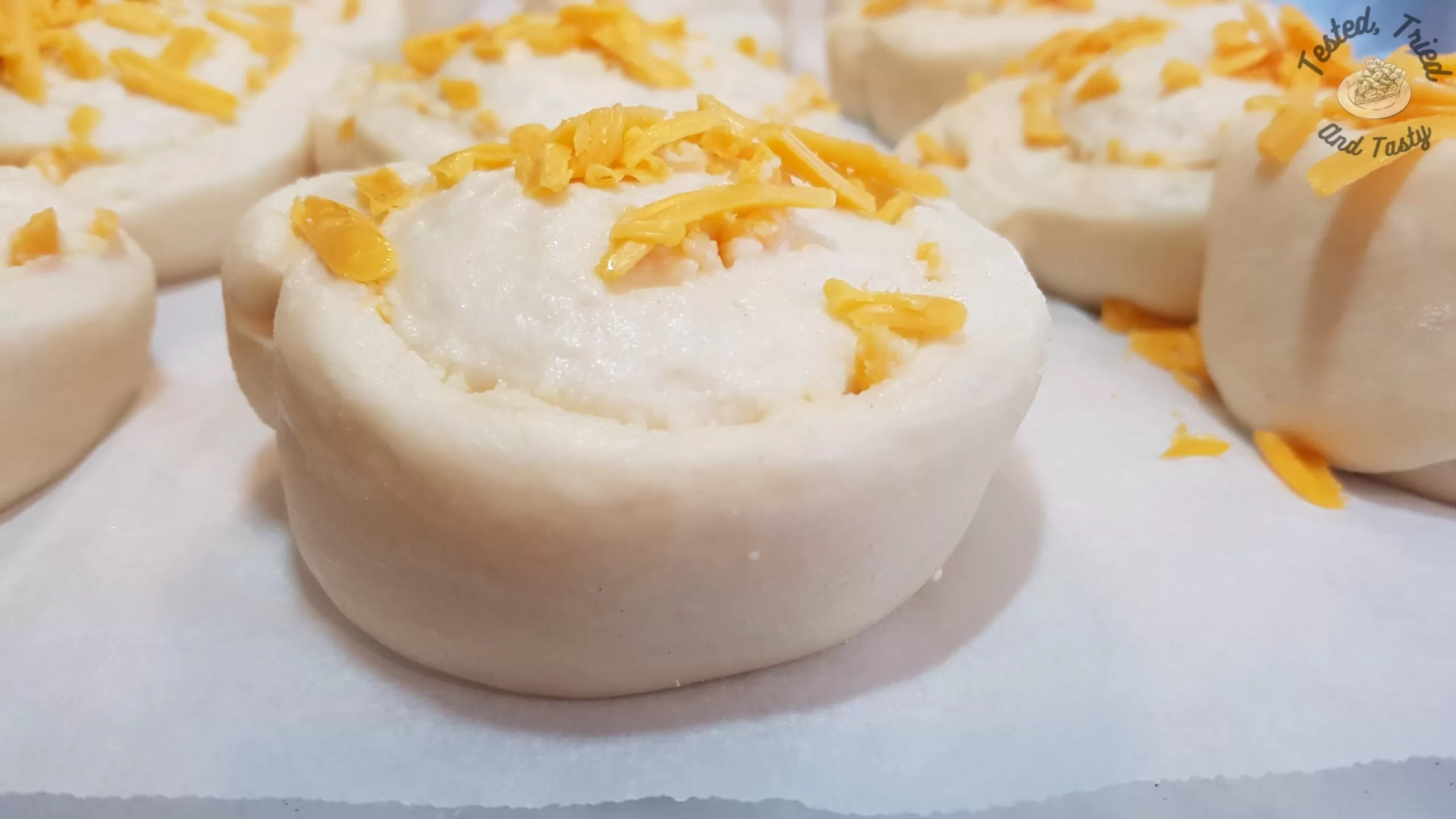 risen garlic cheese buns on parchment paper on a baking sheet